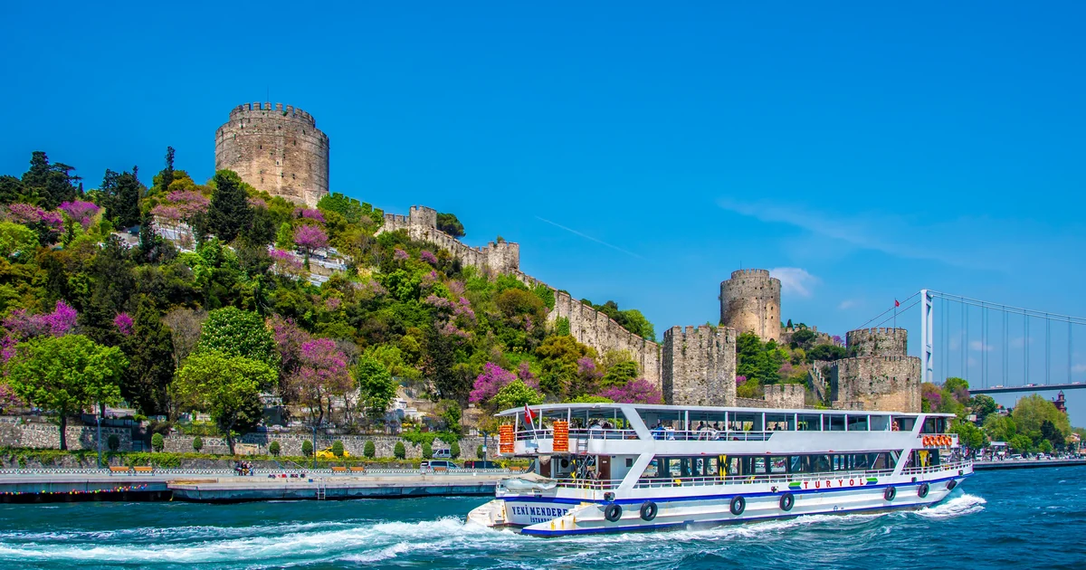 Bosphorus cruise boat passing Rumeli Fortress and the Bosphorus Bridge in Istanbul